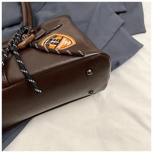 Details einer braunen Leder-Tragetasche mit Metallfüßen und Vintage-Abzeichen
