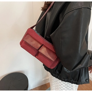 Detail of dark red suede baguette bag featuring front flap pockets and slim shoulder strap