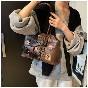 Detailansicht der braunen Vintage-Tasche mit Retro-Patches und dekorativen Anhängern