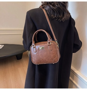 Detailed back view of a brown vintage leather handbag with metal logo and shoulder strap