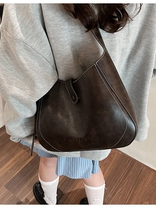 Brown leather underarm bucket bag with white contrast stitching and minimalist flap design