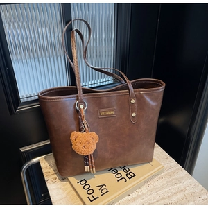 Detail einer braunen PU-Leder Tragetasche mit goldenem Logo und Bären-Anhänger