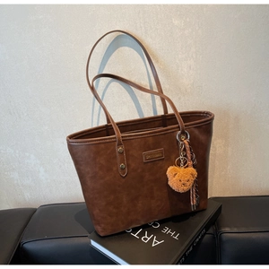 Detailaufnahme einer braunen Vintage-Einkaufstasche mit Lederstruktur und Bärenanhänger