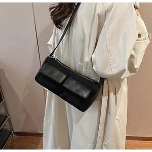 Detail of black nylon crossbody bag with double front pockets on a model in a trench coat