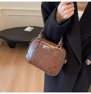 Detailed close-up of brown vintage leather crossbody bag with silver metal plaque logo