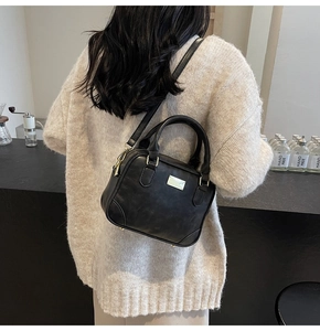 Close-up of black retro Boston handbag showing matte PU leather and silver metal plaque