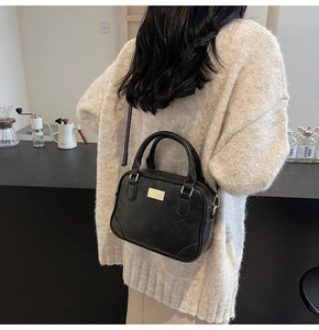 Detail of black leather handbag with gold metal plaque shown in a cozy cafe setting
