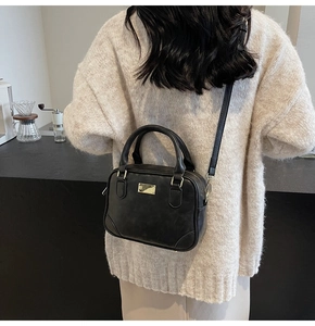 Detail of a vintage black crossbody square bag with gold hardware on a model back view