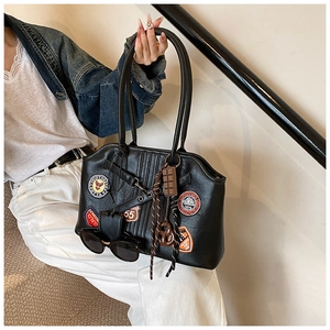 Detail der schwarzen Ledertasche mit Vintage-Abzeichen, Anhängern und langen Griffen