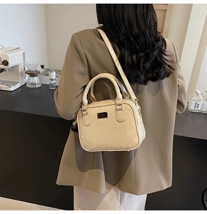 Detail of a beige PU leather crossbody bag with metal accent and sturdy handles