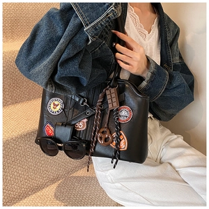 Detailansicht der schwarzen Handtasche mit Vintage-Badges und kreativen Anhängern