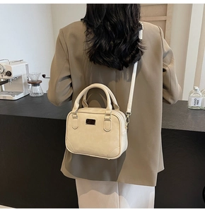 Detail showing beige leather structured handbag with crossbody strap and metallic logo plate
