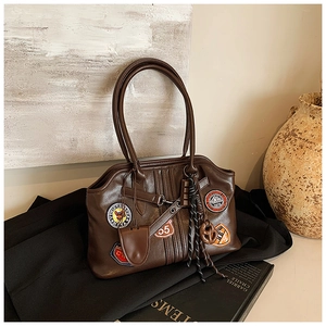 Detailansicht der braunen Retro-Tasche mit bestickten Aufnähern und Lederquasten-Elementen
