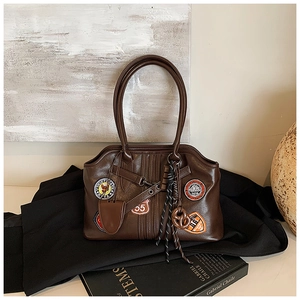Detail der braunen Lederhandtasche mit Retro-Renn-Aufnähern und gewebten Anhängern