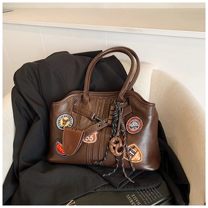 Detail der dunkelbraunen Vintage-Umhängetasche mit Patches und Herzanhänger auf Stuhl
