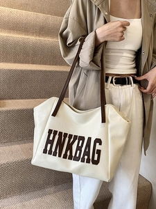 Borsa tote beige di tendenza con manici marroni e logo indossata da una modella