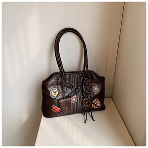 Detailaufnahme der braunen Vintage-Tasche mit aufgestickten Abzeichen und Anhänger