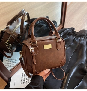Detail view of dark brown PU leather handbag with golden logo plate and metal hardware