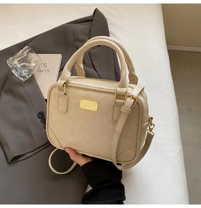 Detail of a creamy beige pillow bag with gold hardware on a grey blazer and white bedding