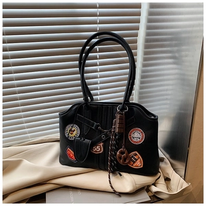 Details der schwarzen Vintage-Schultertasche mit Stick-Patches und kreativen Anhängern