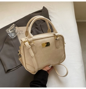 Detail of a beige leather handbag with gold metal clasp on grey blazer background