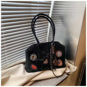 Detailansicht der schwarzen Leder-Tragetasche mit Retro-Stickereien und Schokoladen-Anhänger