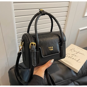Detailed shot of glossy black leather handbag with gold metal logo and handle