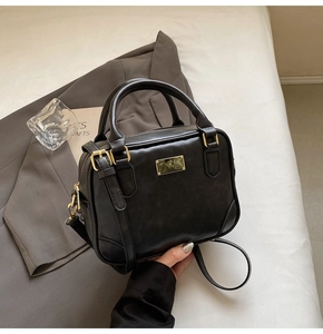 Detail of a black leather Boston bag with gold hardware placed on a gray suit jacket