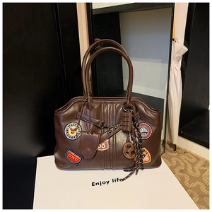 Detail der dunkelbraunen Ledertasche mit Vintage-Patches und niedlichen Anhängern