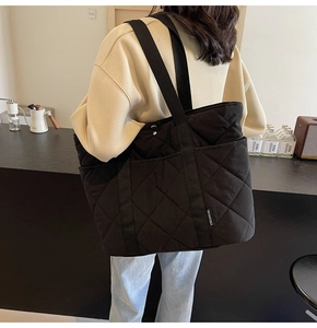 Détail du sac fourre-tout noir matelassé avec motif losanges et étiquette logo de marque