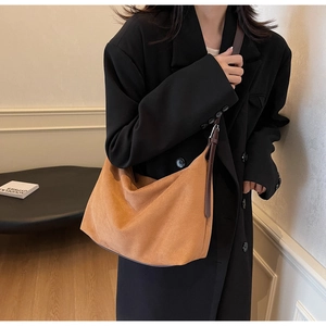 Nahaufnahme der karamellbraunen Wildledertasche mit Lederriemen an einem Model im schwarzen Anzug