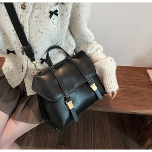 Close-up of black vintage leather satchel with gold buckles and crossbody strap