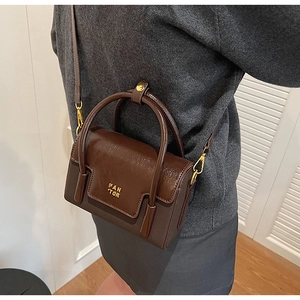 Detail of dark brown leather handbag with gold logo and adjustable shoulder strap
