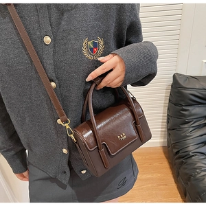 Close-up of glossy brown leather square handbag with golden Pan Tor metallic logo