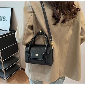 Close-up of black PU leather square bag with PAN 'TOR gold lettering and top handle