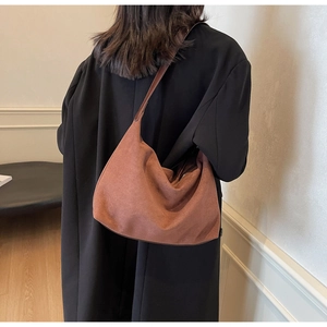 Detail der braunen Hobo-Tasche aus Wildleder mit Schultergurt auf schwarzem Mantel