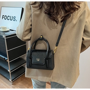 Detailed view of black mini square handbag with PAN 'TOR gold lettering and glossy finish