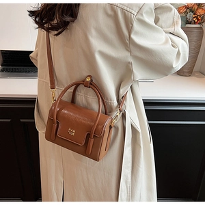 Brown leather crossbody bag with gold FAN TOR logo styled on a beige trench coat