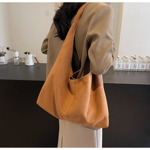 Sac hobo marron en daim porté à l'épaule au style rétro minimaliste dans un café