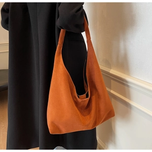 Vue latérale d'un grand sac cabas en daim orange porté par un mannequin sur mur blanc