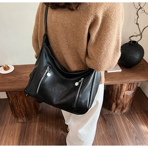 Détail d'un sac hobo noir sur un modèle montrant la texture du cuir et les fermetures éclair