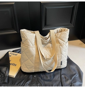 Détail du sac cabas beige matelassé à losanges posé sur une veste en cuir noir
