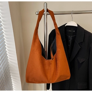 Gros plan du sac cabas en daim orange vif avec large bandoulière et doublure noire