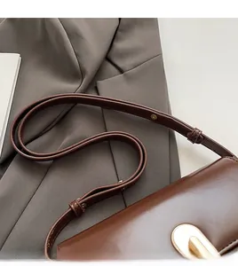 Detail of adjustable shoulder strap and gold oval buckle on dark brown leather crossbody bag