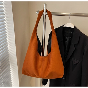 Détail d'un grand sac cabas en daim orange caramel suspendu sur un support métallique
