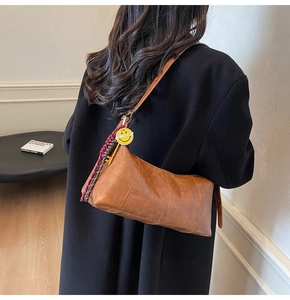 Detail of brown soft leather dumpling bag featuring a yellow Smiley charm and woven strap
