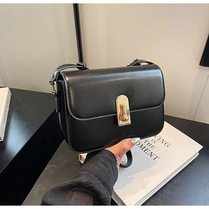 Detail of matte black leather bag featuring a vertical gold metal buckle closure