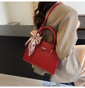 Détail d'un sac à main rouge avec fermoir doré rotatif et foulard en soie à motif de cœurs