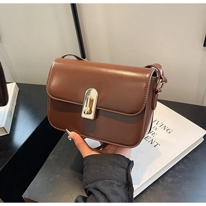 Detail of a chocolate brown crossbody bag featuring a golden metal buckle and smooth leather