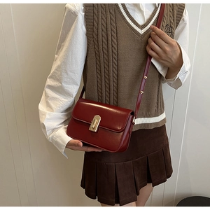 Detail of vintage burgundy leather crossbody bag with golden metal twist-lock and rivets